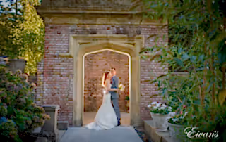 Newlyweds embrace each other beneath a well-lit entryway in the garden.