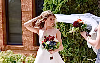 The bride smiles beautifully as her bridesmaids help elegantly arrange her veil.