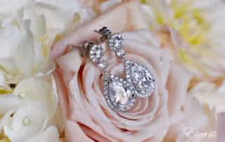 The bride's stunning jewelry effortlessly lays upon a light pink rose that is in her beautiful bouquet.