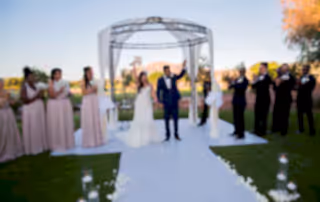 Newlywed Bride and Groom conclude ceremony by raising their arms and greeting guests as husband and wife. Bridesmaids and Groomsmen clap and cheer on either side of the altar as the sun sets.