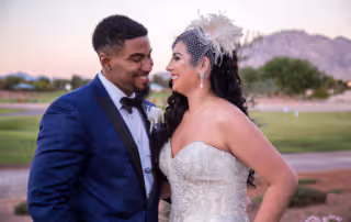 Fashion photographer captures a joyful moment between Bride and Groom at sunset. The Groom is wearing a handsome blue and black color block tuxedo jacket. The Bride is wearing a lovely vintage birdcage visor and drop pearl earrings.