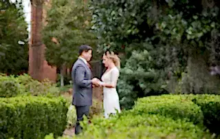 Candid photography of a Bride and Groom holding hands and exchanging words in the garden. Bushes, trees, and wildflowers surround them as they share a private moment.