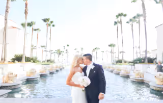 man in black suit kissing woman in white wedding dress near body of water during daytime